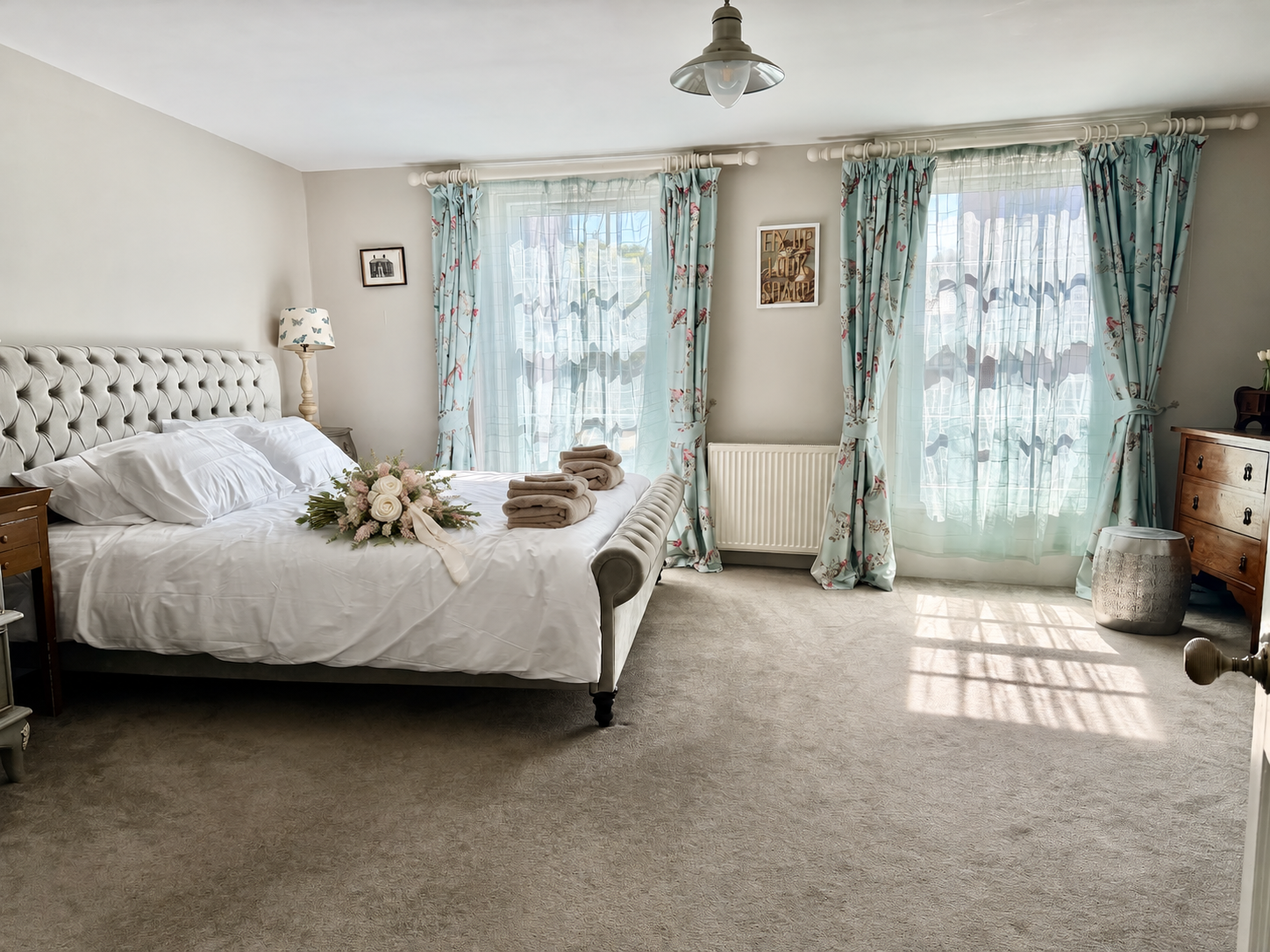 Bridal bedroom with both blue floral-curtained windows and flowers on the bed