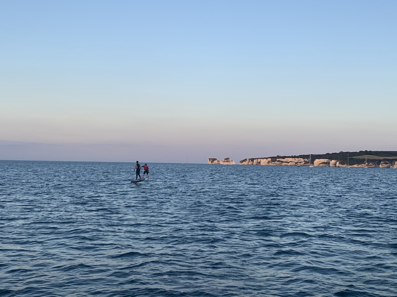 Two people foiling on the sea with the chalk cliffs of Old Harry Rocks in the distance