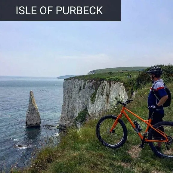 Mountain biker with an orange bike overlooking the chalk cliffs of the Jurassic Coast
